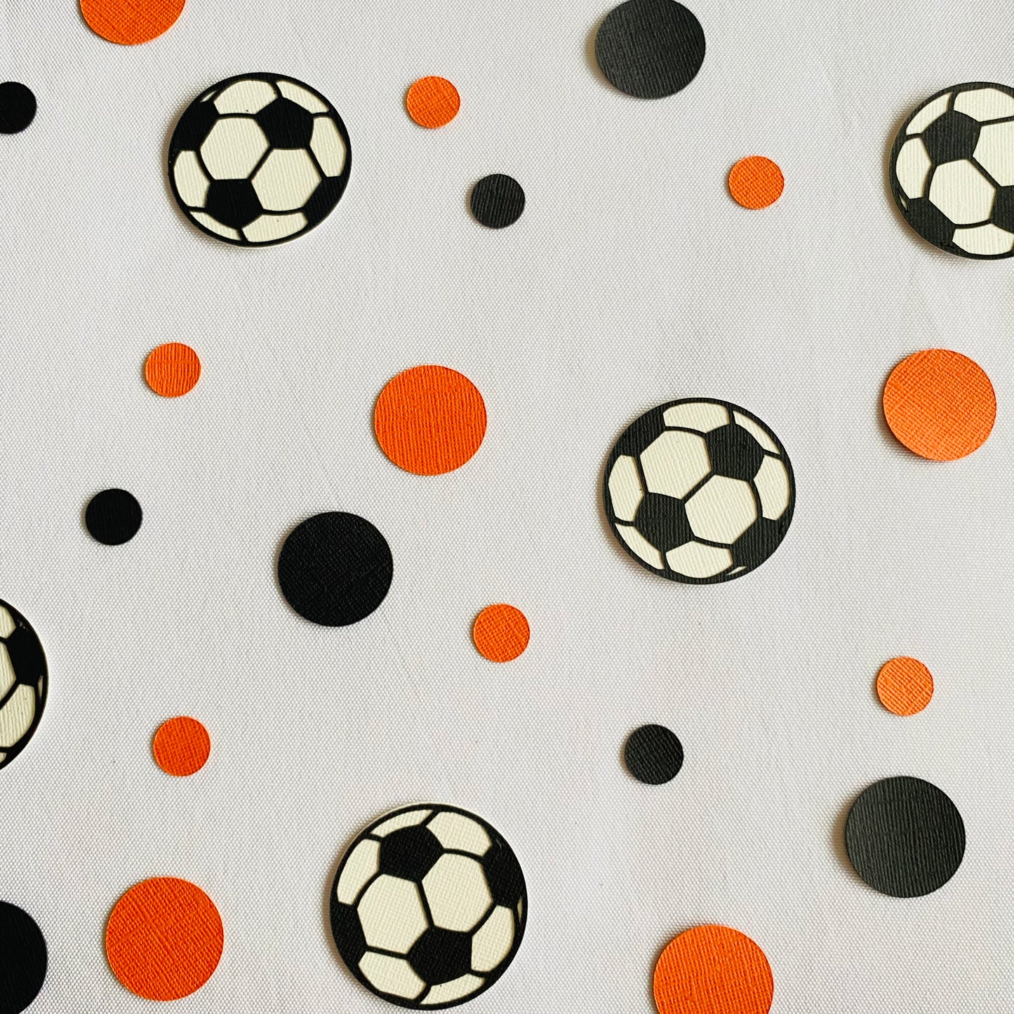 Orange and black paper round discs with soccer ball paper discs  scattered across a white table.
