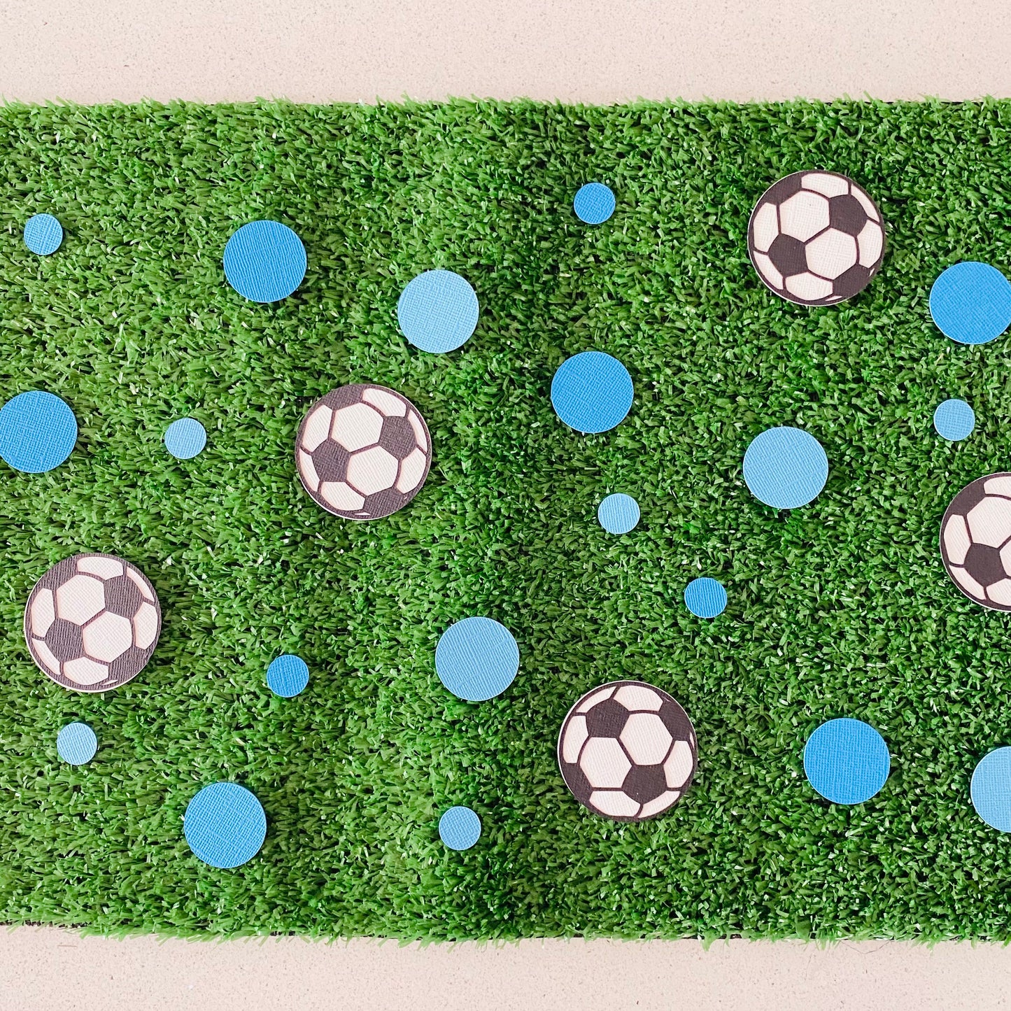 Large and small blue paper round discs with soccer ball paper discs  scattered across green grass.