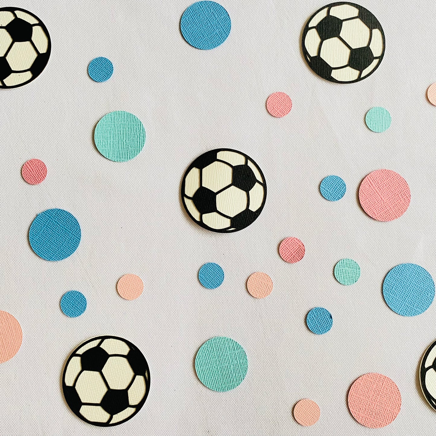 Large and small pink and blue paper round discs with soccer ball paper discs scattered across a white table.