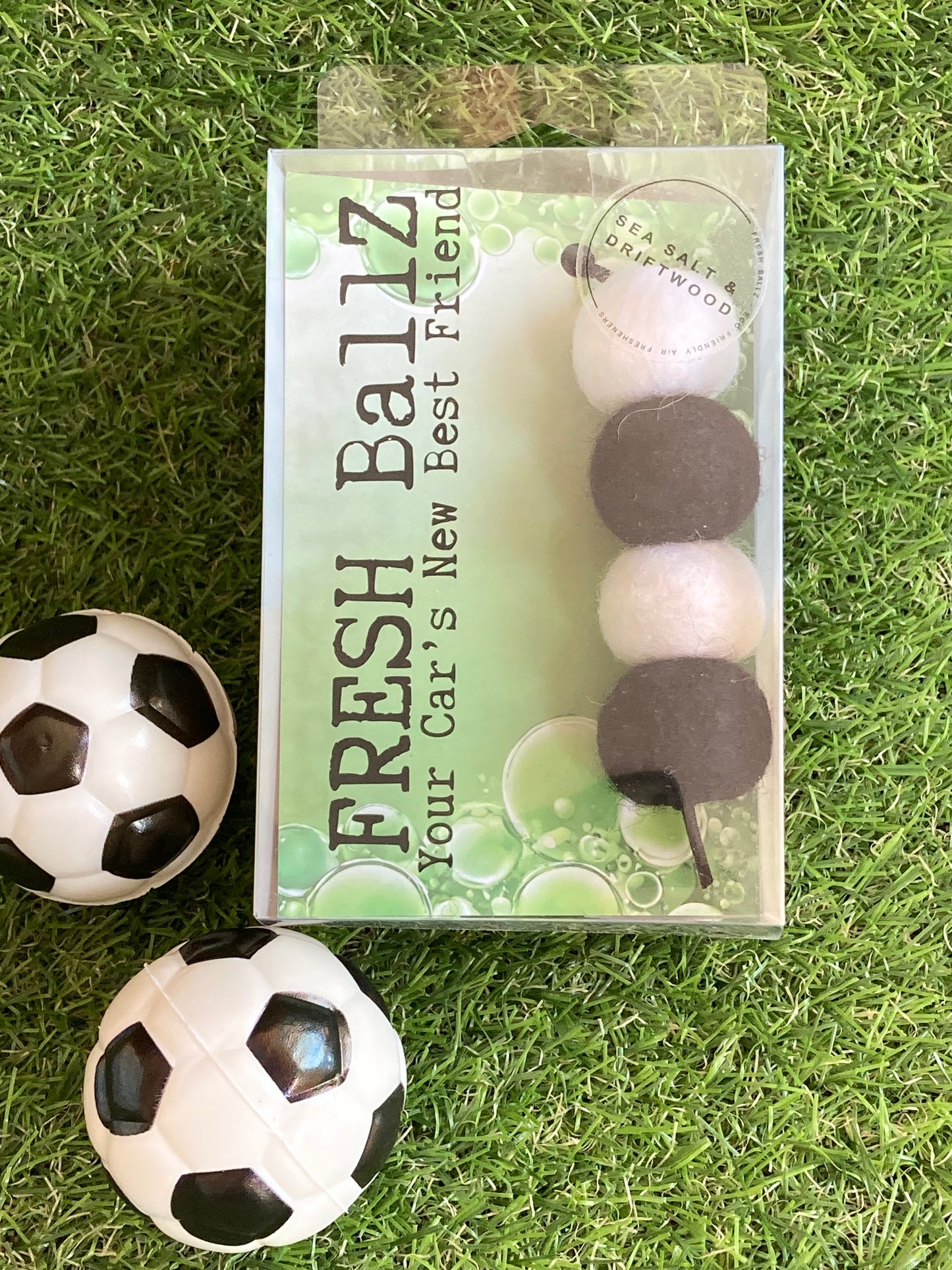 Black and white woolen balls in clear plastic case to hang in the car laying on grass with soccer ball props