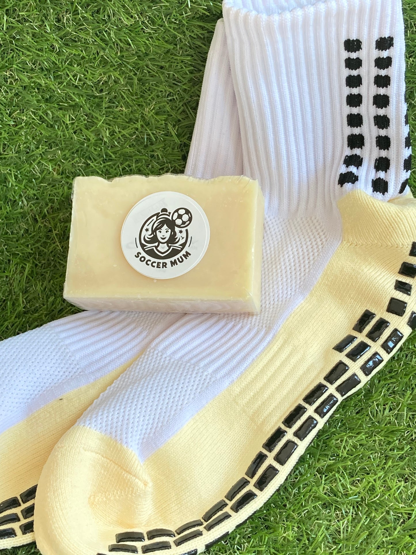 Block of cream soap with a soccer mum logo laying on  pair of clean socks. All on a background of grass.