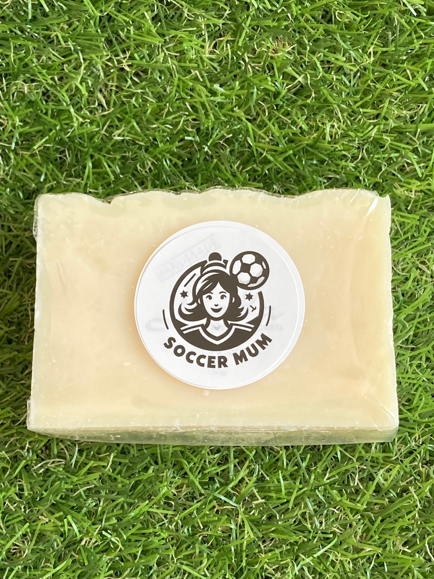 Block of cream soap with a soccer mum logo laying on a background of grass.
