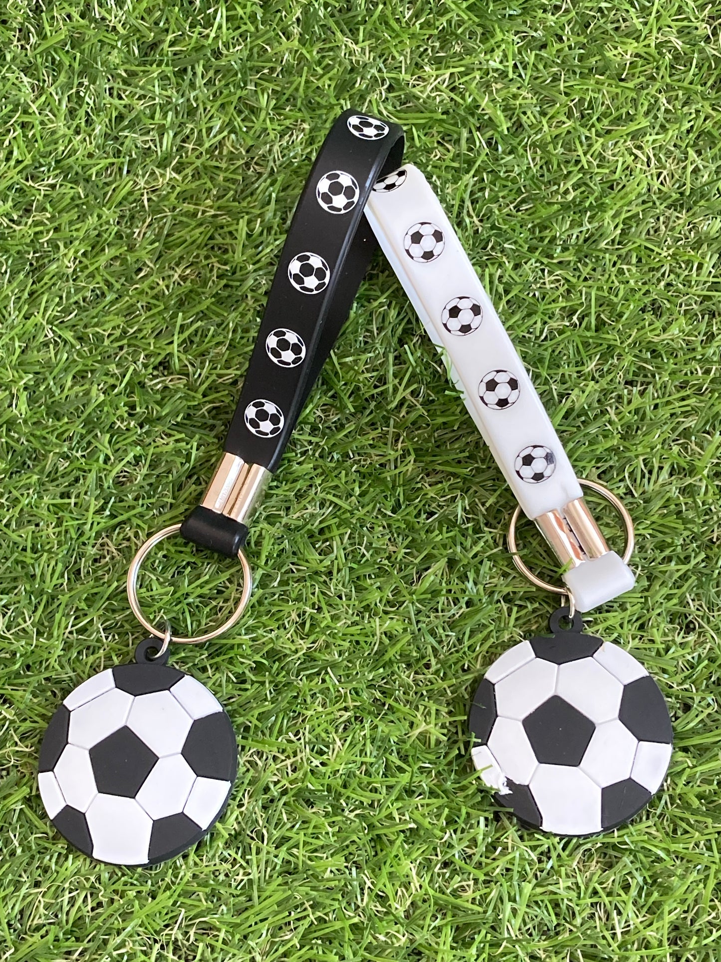 Black and white key chain with hanging soccer balls sitting side by side on the grass