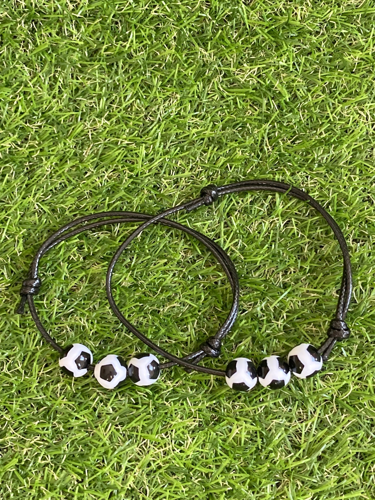 Up close image of Faux leather bracelet with 3 plastic soccer ball charms laying on soccer grass.