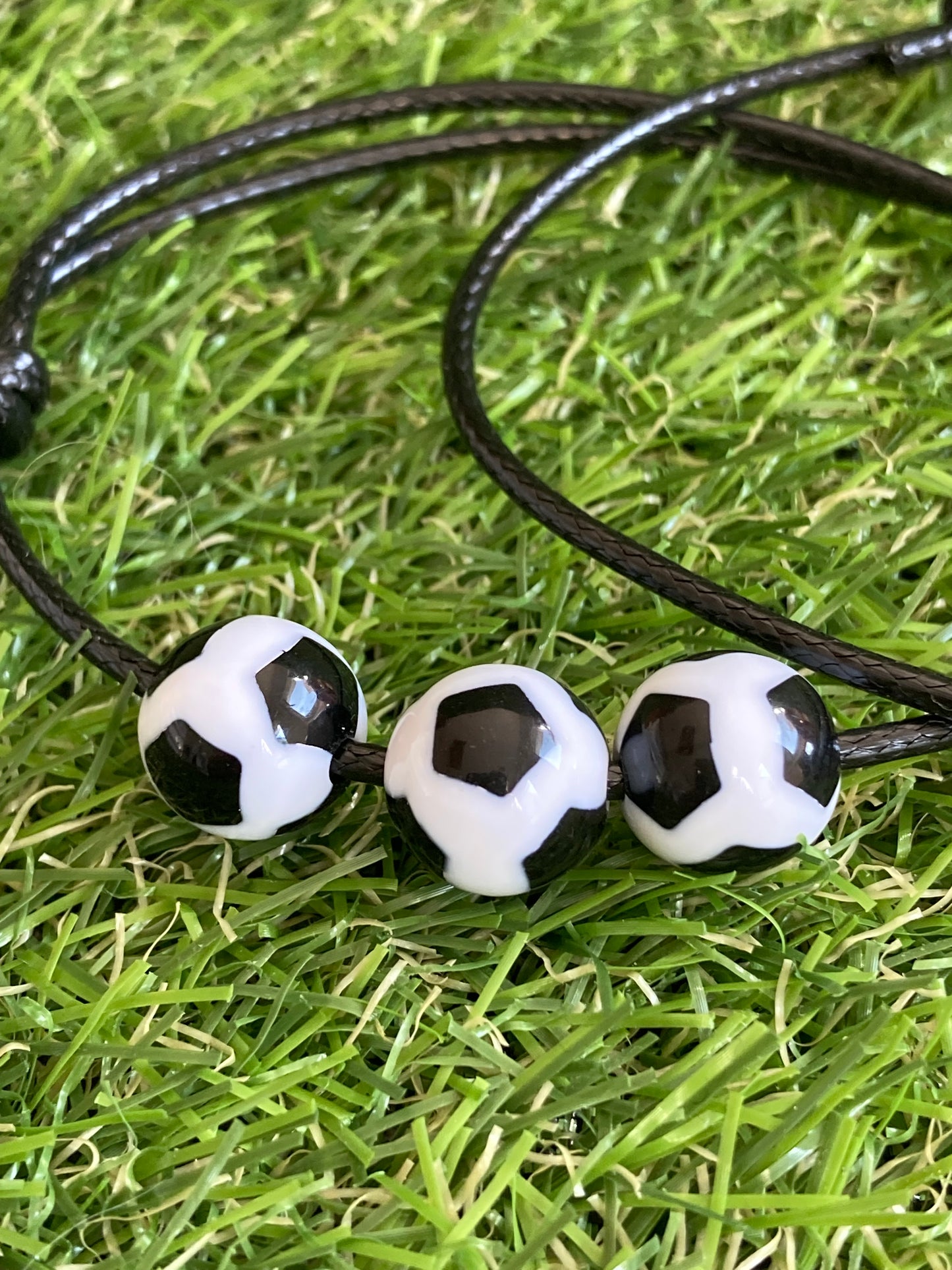 Up close image of Faux leather bracelet with 3 plastic soccer ball charms laying on soccer grass.