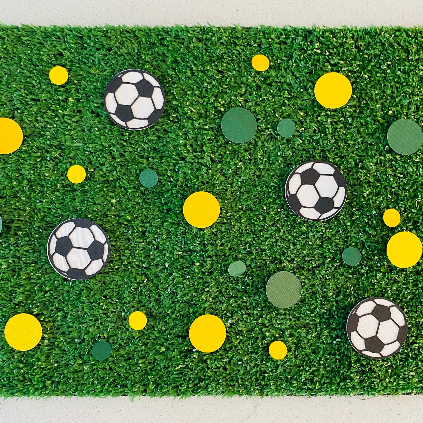 Soccer ball confetti with small and large green and gold circle confetti scattered across green grass