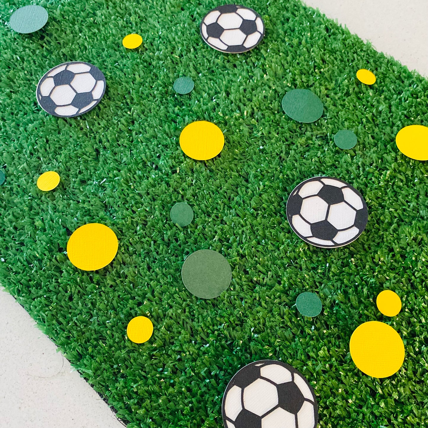 Soccer ball confetti with small and large green and gold circle confetti scattered across green grass