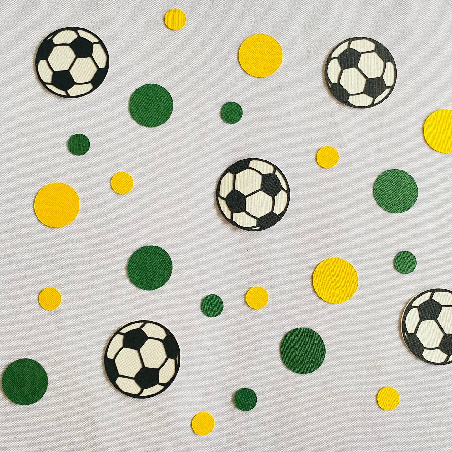 Soccer ball confetti with small and large green and gold circle confetti scattered across green grass