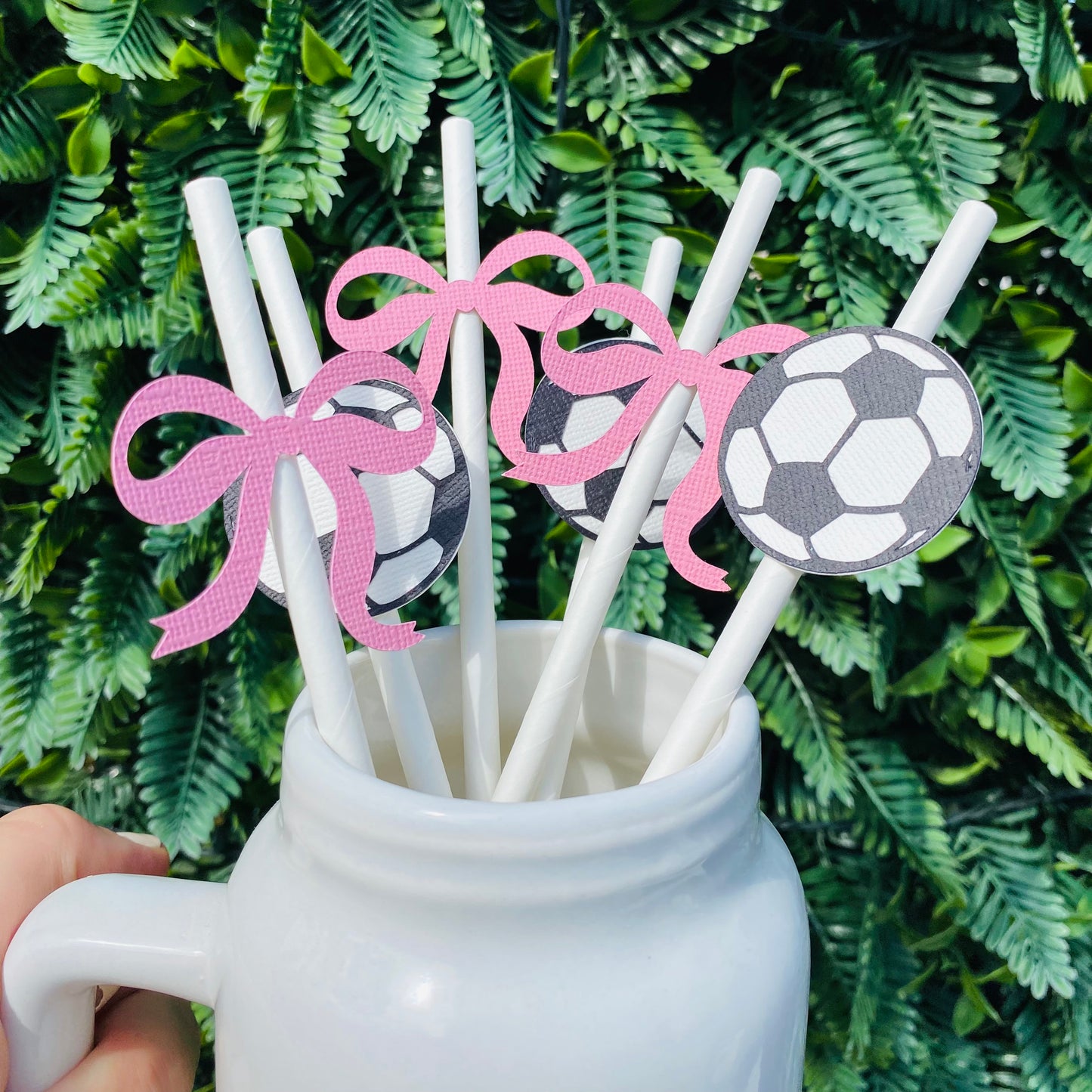 White straws topped with black and white soccer ball paper straw toppers and pink bow paper straw toppers displayed in a mason jar.