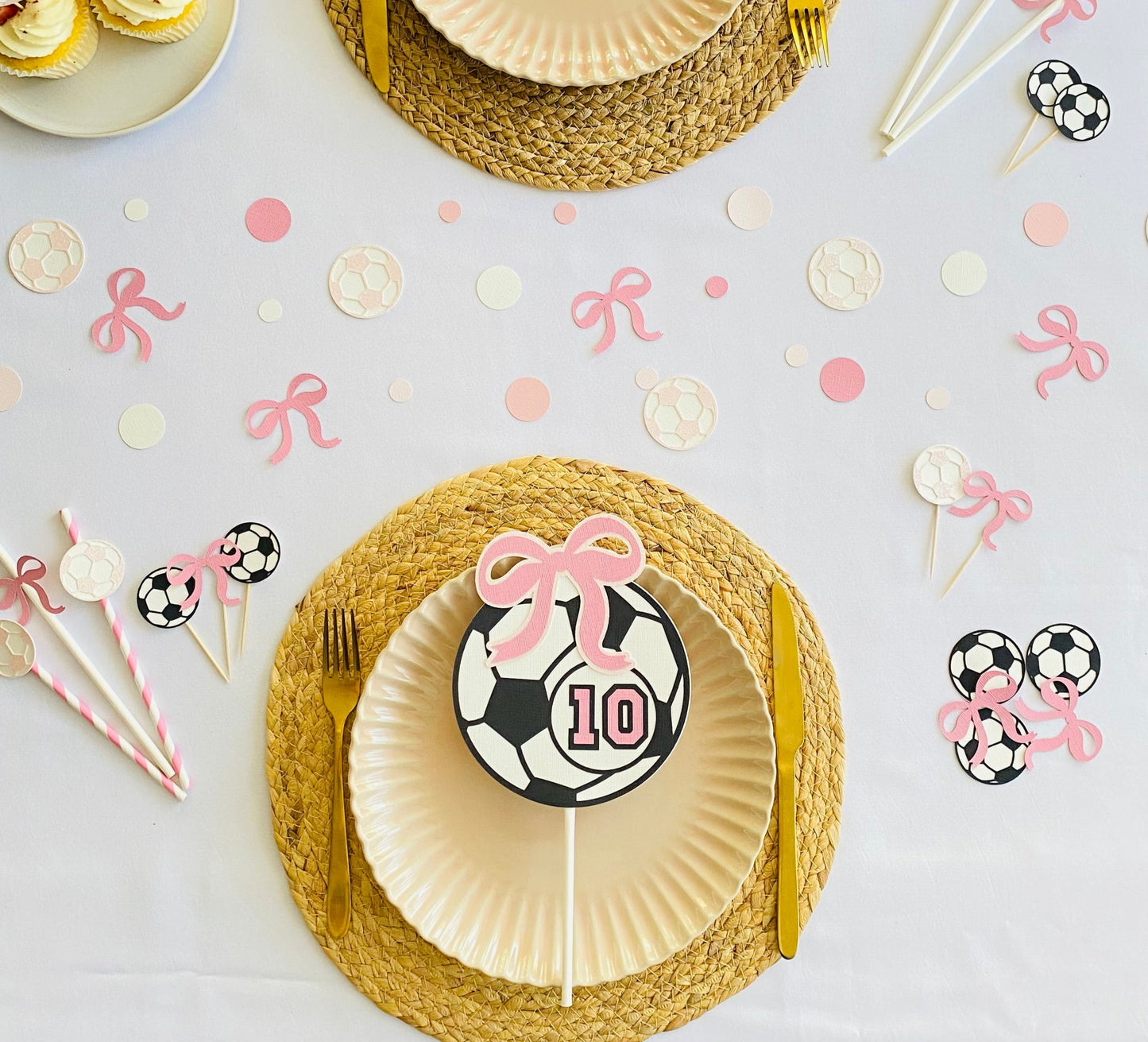 Black and white soccer ball cake topper with pink bow laying on a plate surrounded by pink and white soccer ball  themes table scatters.