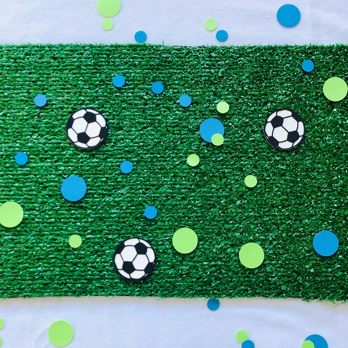Round shape table scatters made from paper in blue and green with black and white soccer balls scattered across green grass.