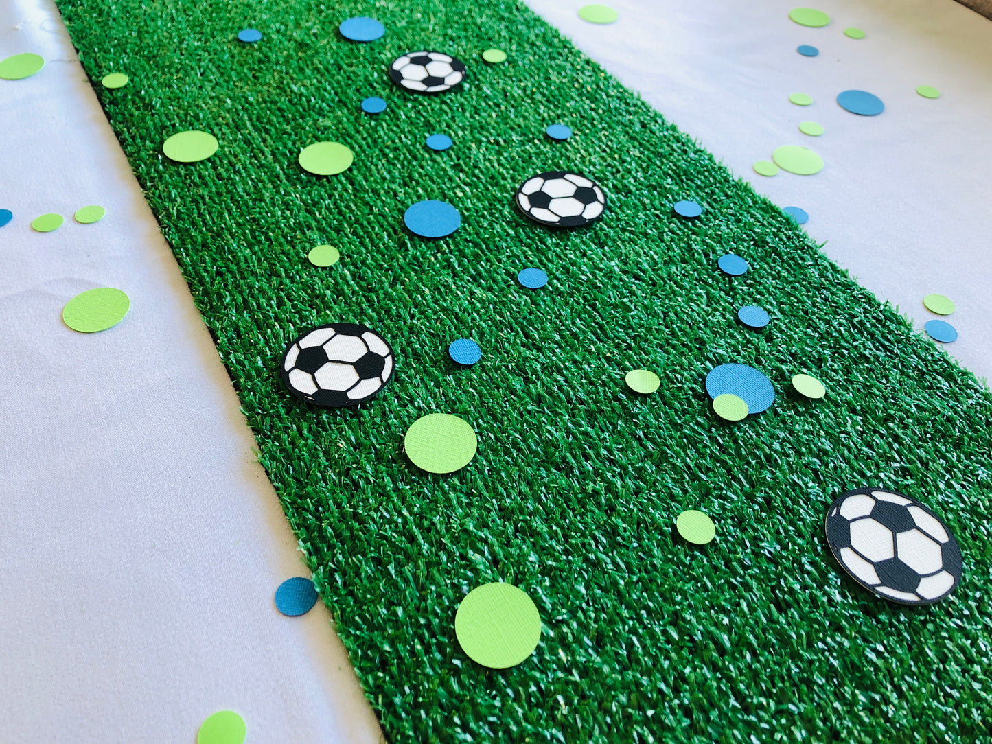 Round shape table scatters made from paper in blue and green with black and white soccer balls scattered across green grass.