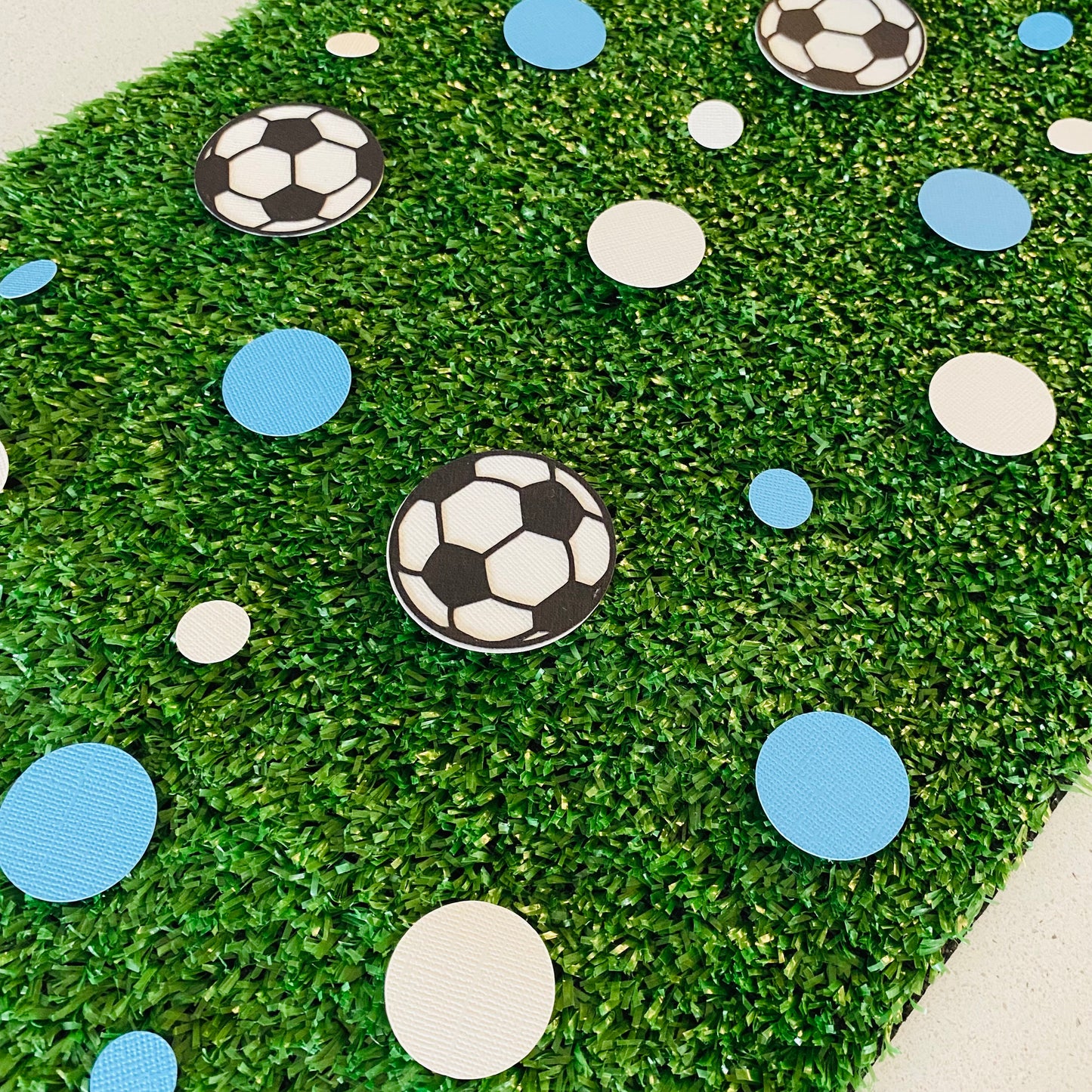 Blue and white round paper cutouts with soccer ball cutouts spread on synthetic grass