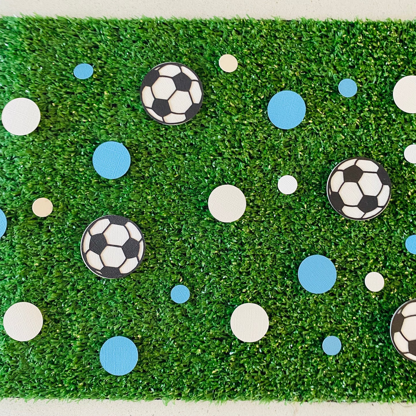 Blue and white round paper cutouts with soccer ball cutouts spread on synthetic grass