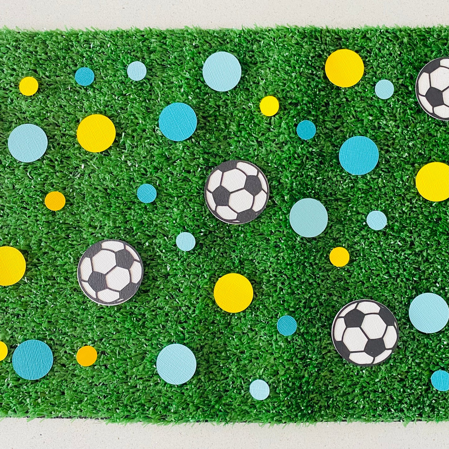 Yellow and blue round paper discs with black and white paper soccer balls scattered across synthetic grass