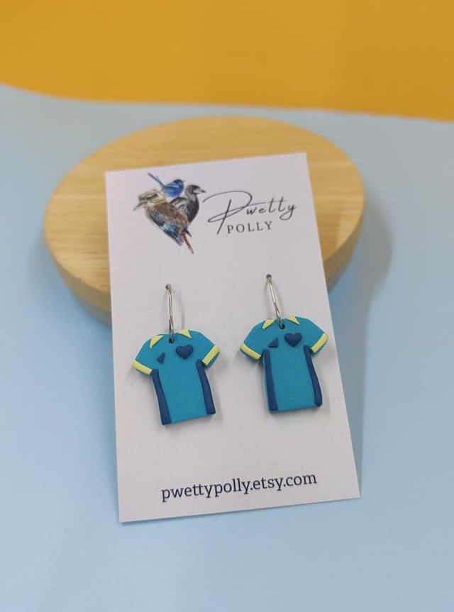 Teal and yellow Matilda shirt earrings on a earring card with a yellow background