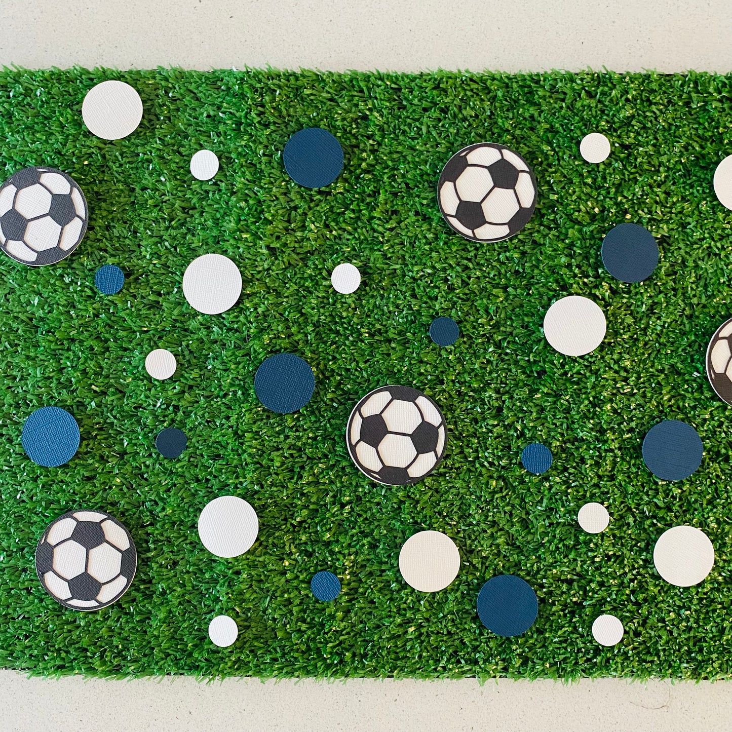 Blue and white round paper cutouts with soccer ball cutouts spread on synthetic grass