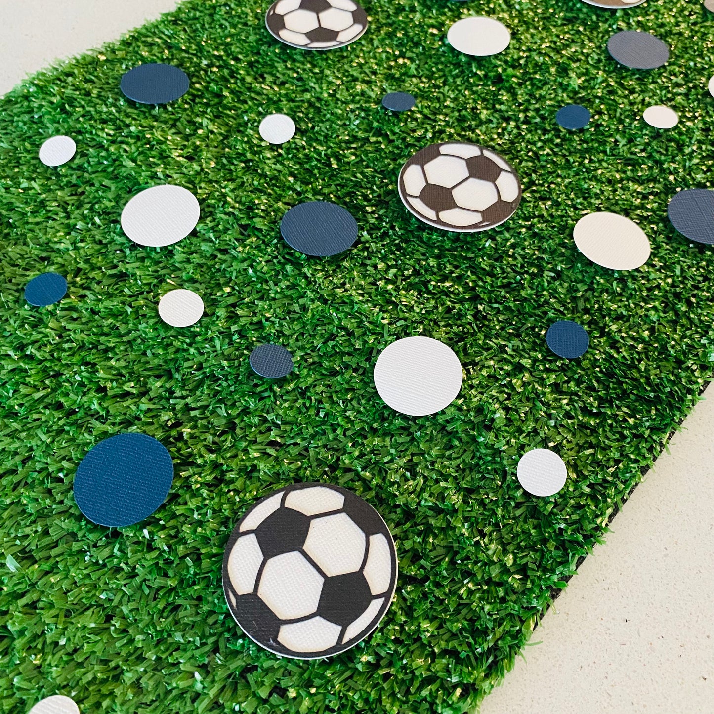 Blue and white round paper cutouts with soccer ball cutouts spread on synthetic grass