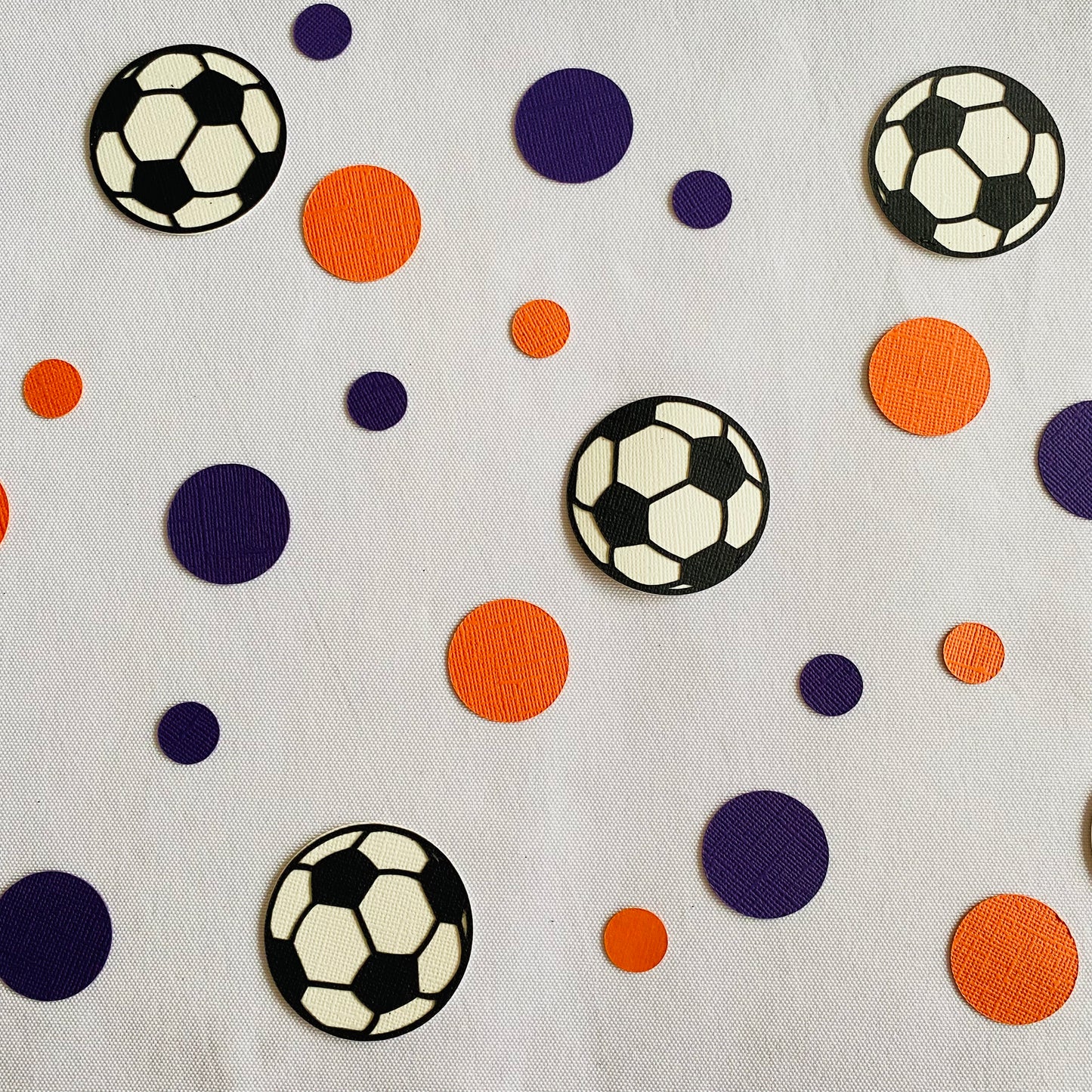 Blue and orange round paper cutouts with soccer ball cutouts spread on synthetic grass