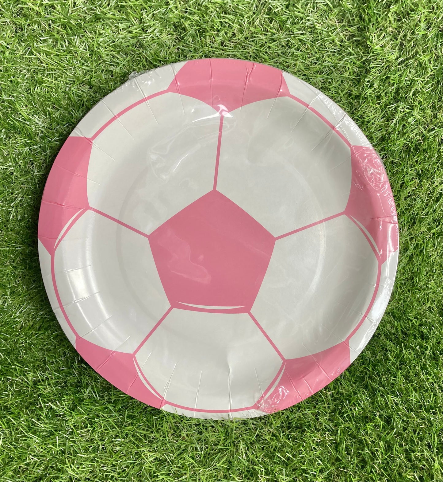 Pink soccer ball theme paper cake plate displayed on astro turf green grass.