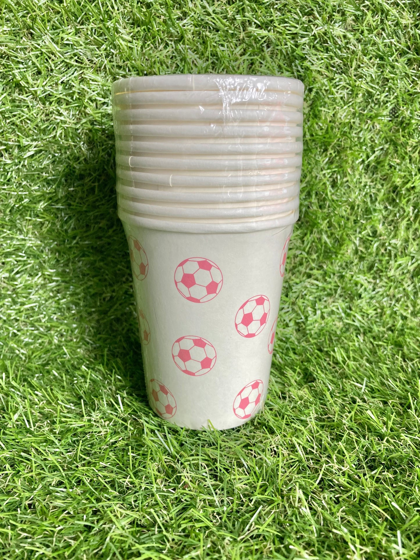 Pink soccer ball theme paper cups displayed on astro turf green grass.