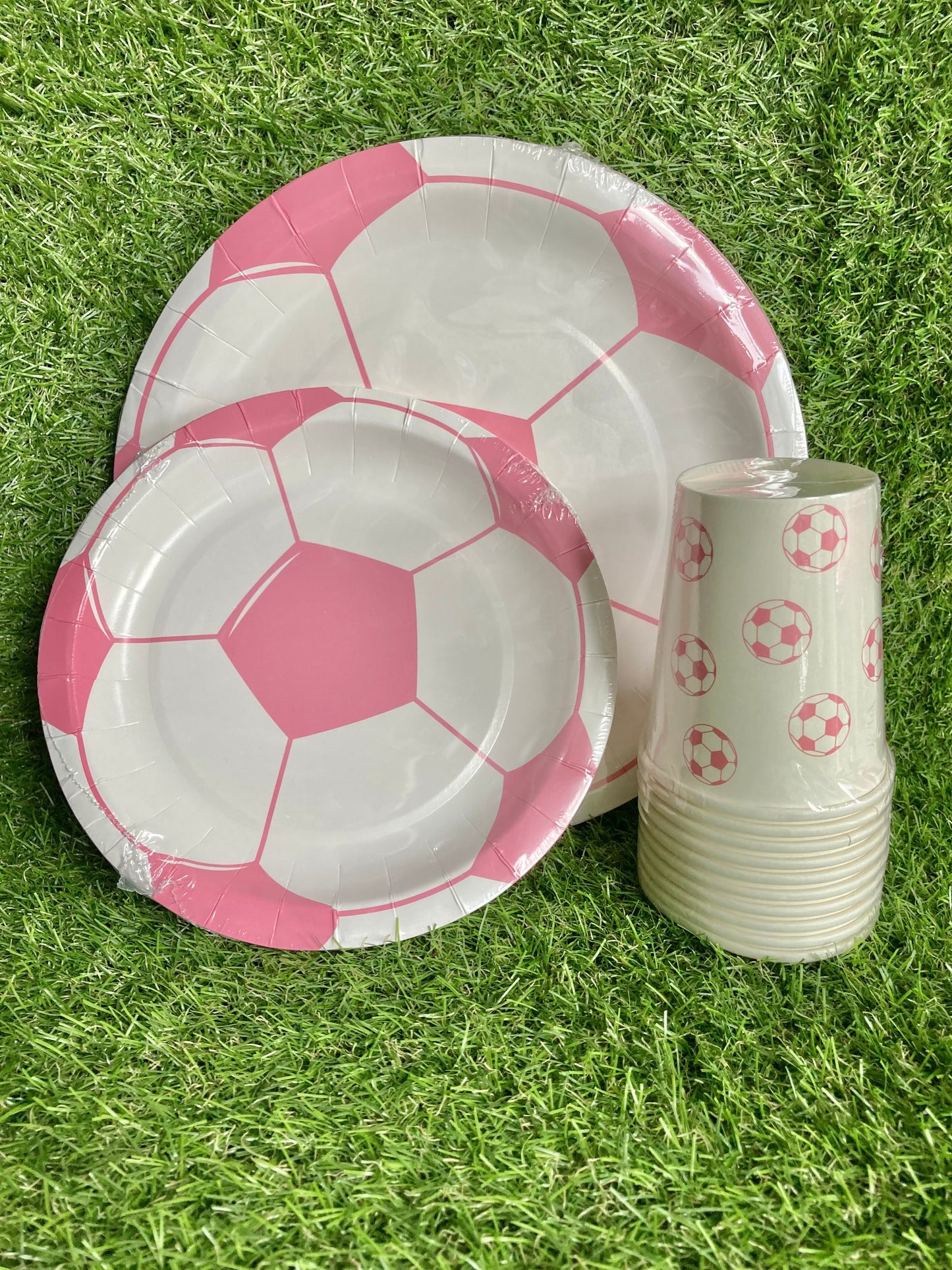 Pink Soccer Ball Paper Plates and paper cups displayed as a bundle on astro turf grass.