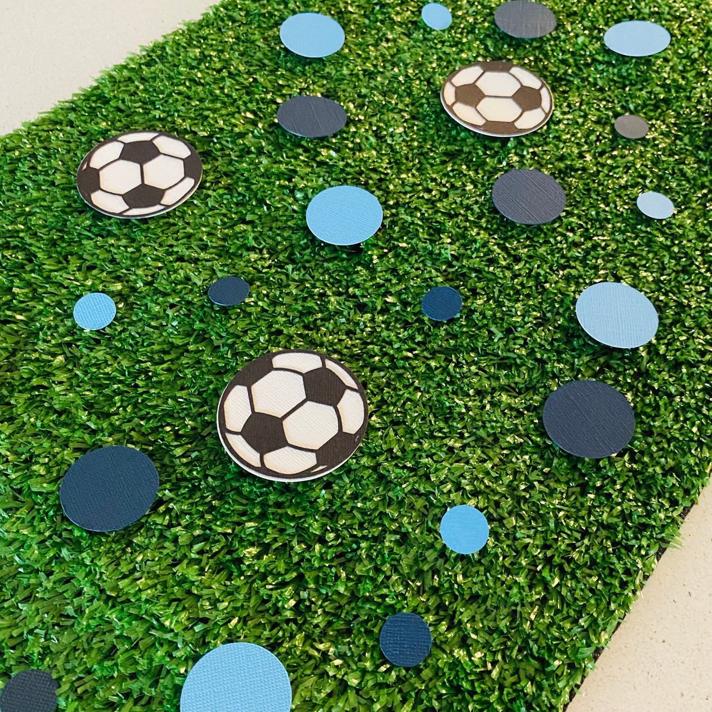 Dark Blue and Light Blue round paper cutouts with soccer ball cutouts spread on synthetic grass