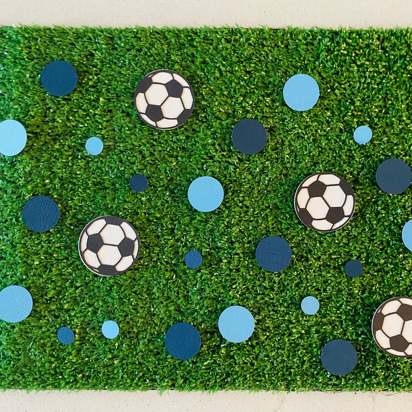 Dark Blue and Light Blue round paper cutouts with soccer ball cutouts spread on synthetic grass