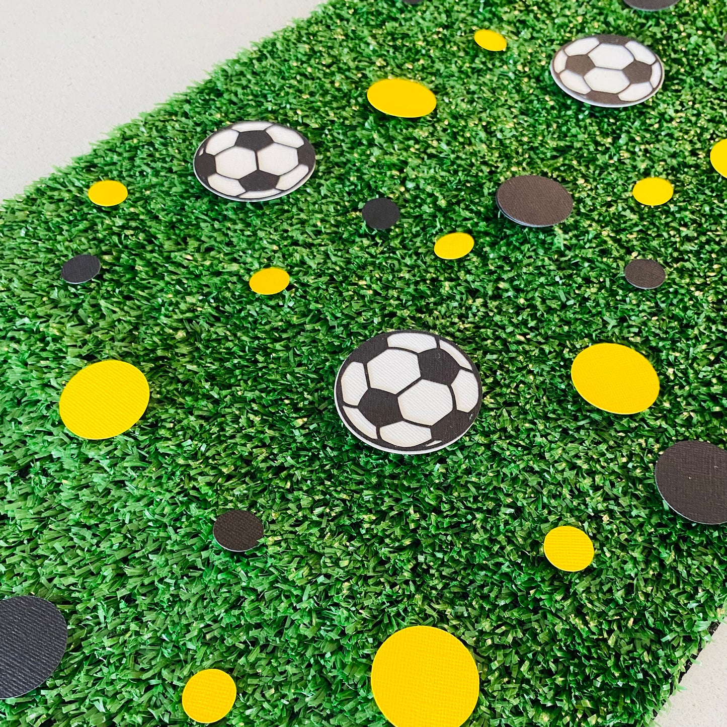 Yellow and Black small and large papercut circles with black and white soccer balls scattered across synthetic grass.