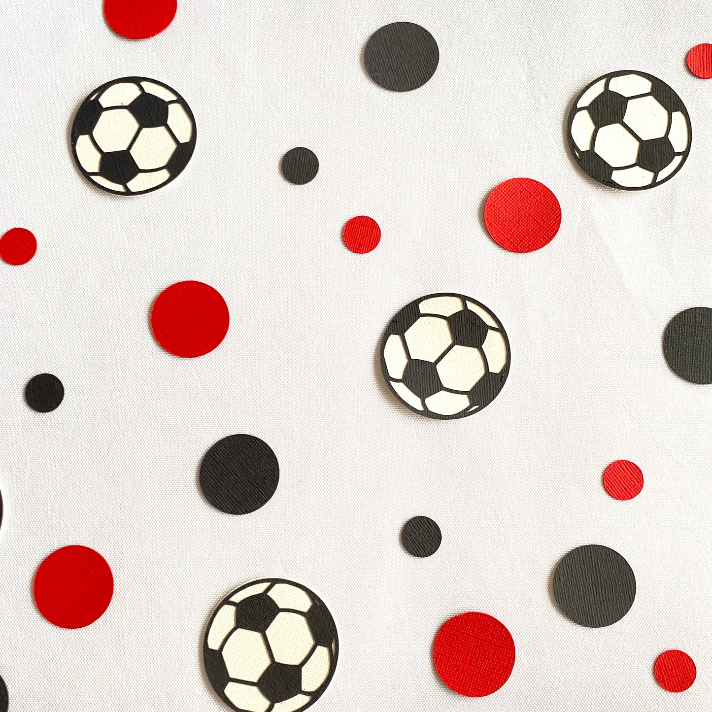 Red and black paper round discs with soccer ball paper discs  scattered across green grass.