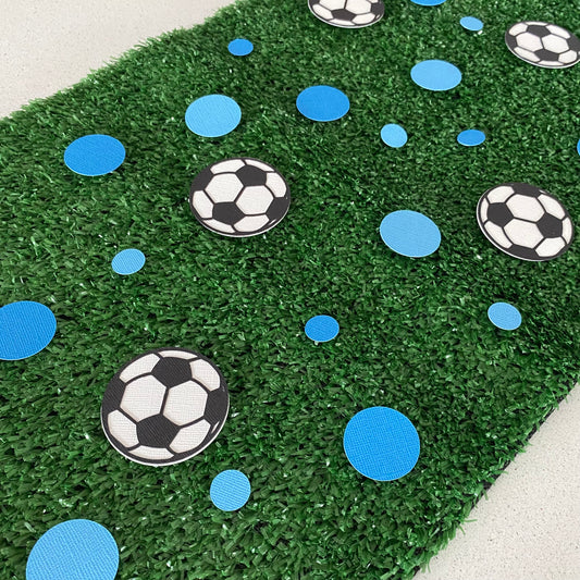 Large and small blue paper round discs with soccer ball paper discs  scattered across green grass.