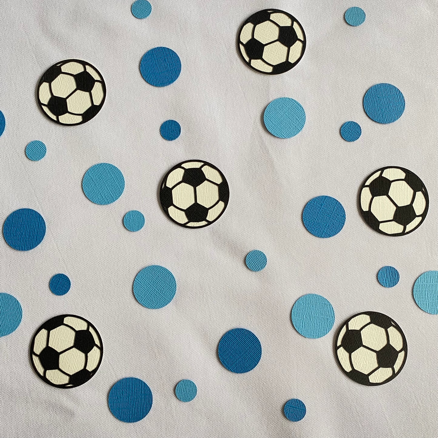 Large and small blue paper round discs with soccer ball paper discs  scattered across a white table