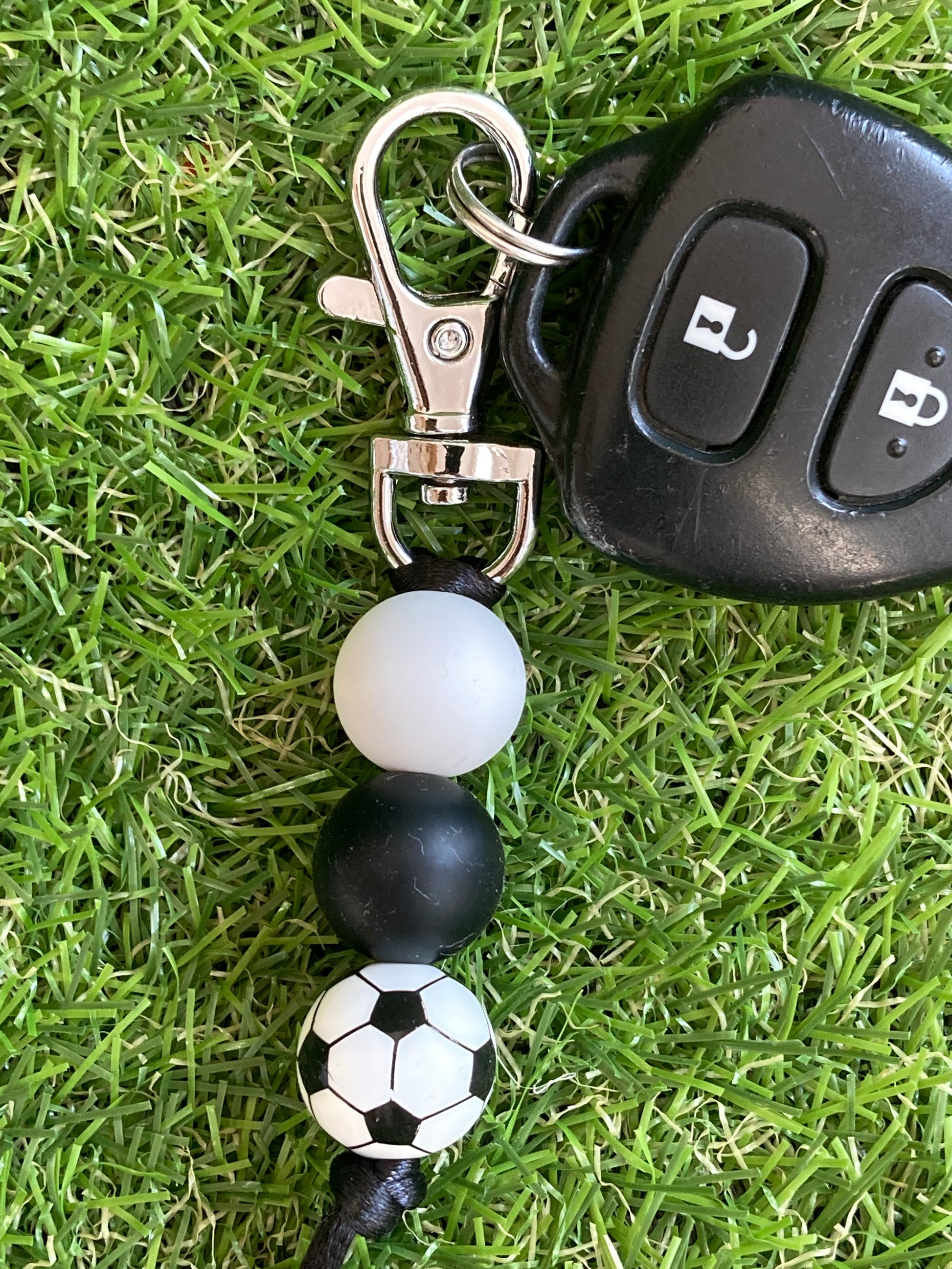 Beaded keychain that is black and white with a soccer ball bead attached to a key lying on grass.