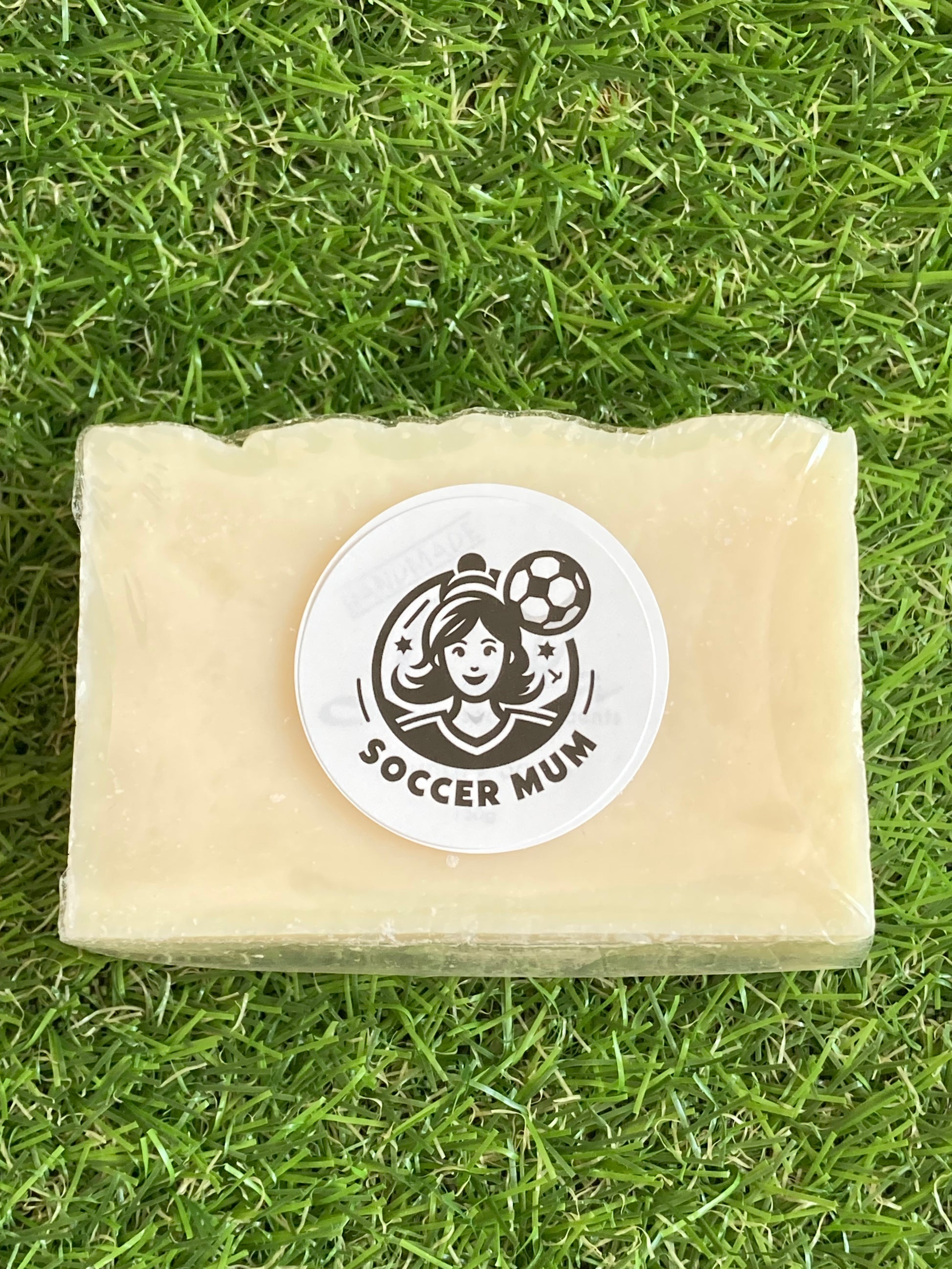 Block of cream soap with a soccer mum logo laying on a background of grass.