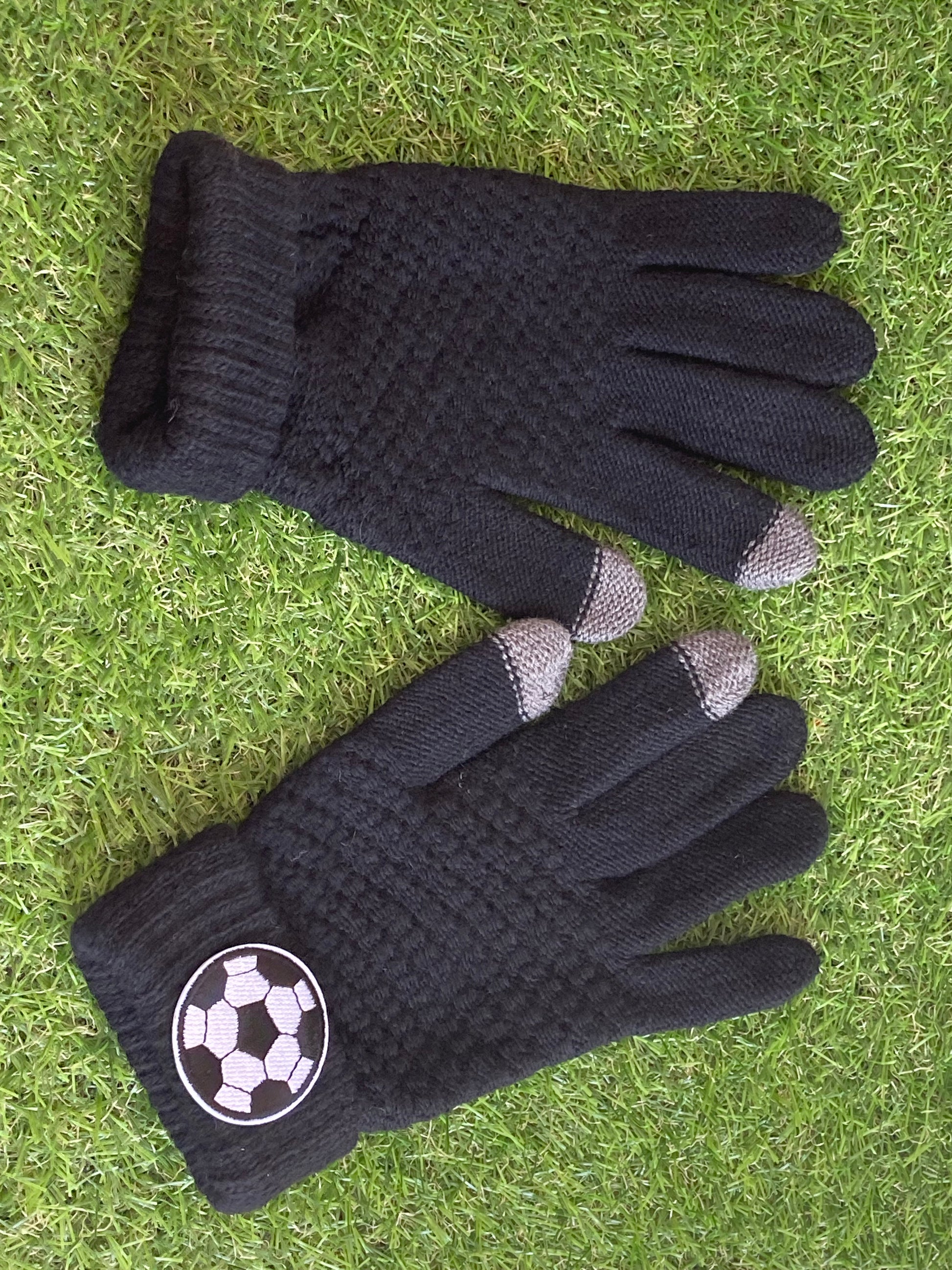Pair of black gloves lying side by side on the grass with a soccer ball patch