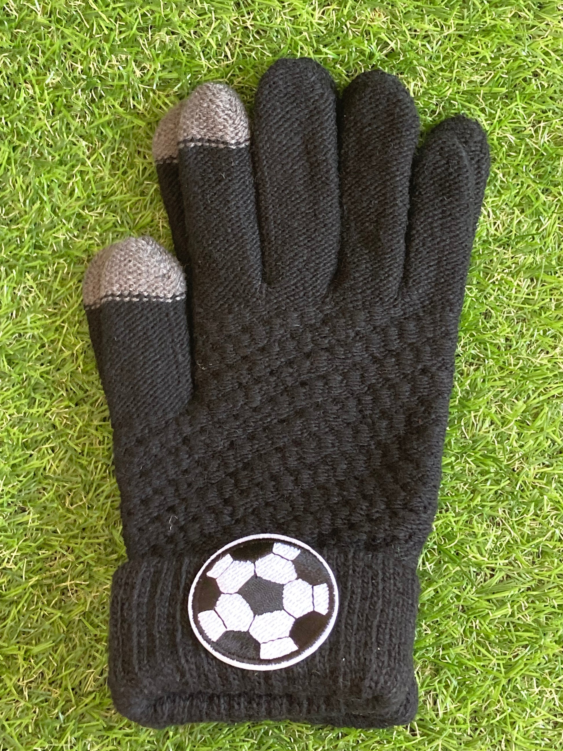 Pair of black gloves lying side by side on the grass with a soccer ball patch