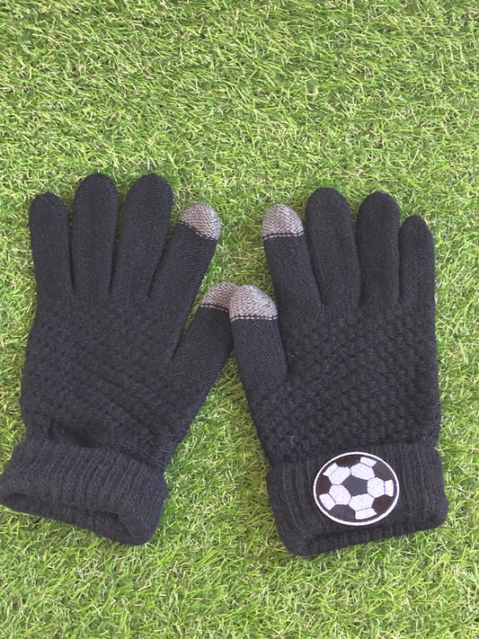 Pair of black gloves lying side by side on the grass with a soccer ball patch