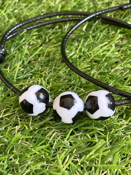 Up close image of Faux leather bracelet with 3 plastic soccer ball charms laying on soccer grass.