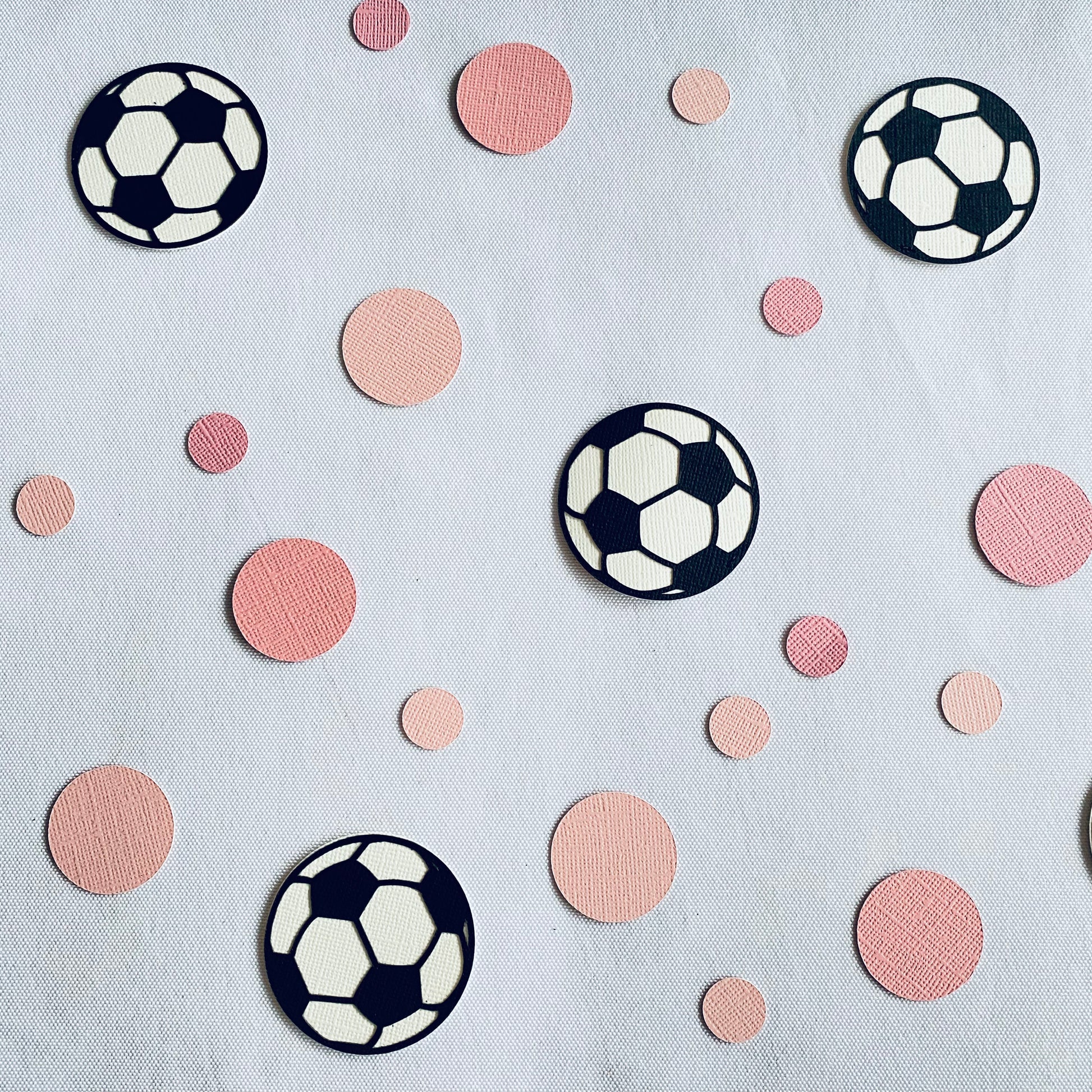 Large and small pink paper round discs with soccer ball paper discs  scattered across a white table.