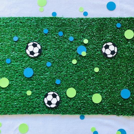 Round shape table scatters made from paper in blue and green with black and white soccer balls scattered across green grass.