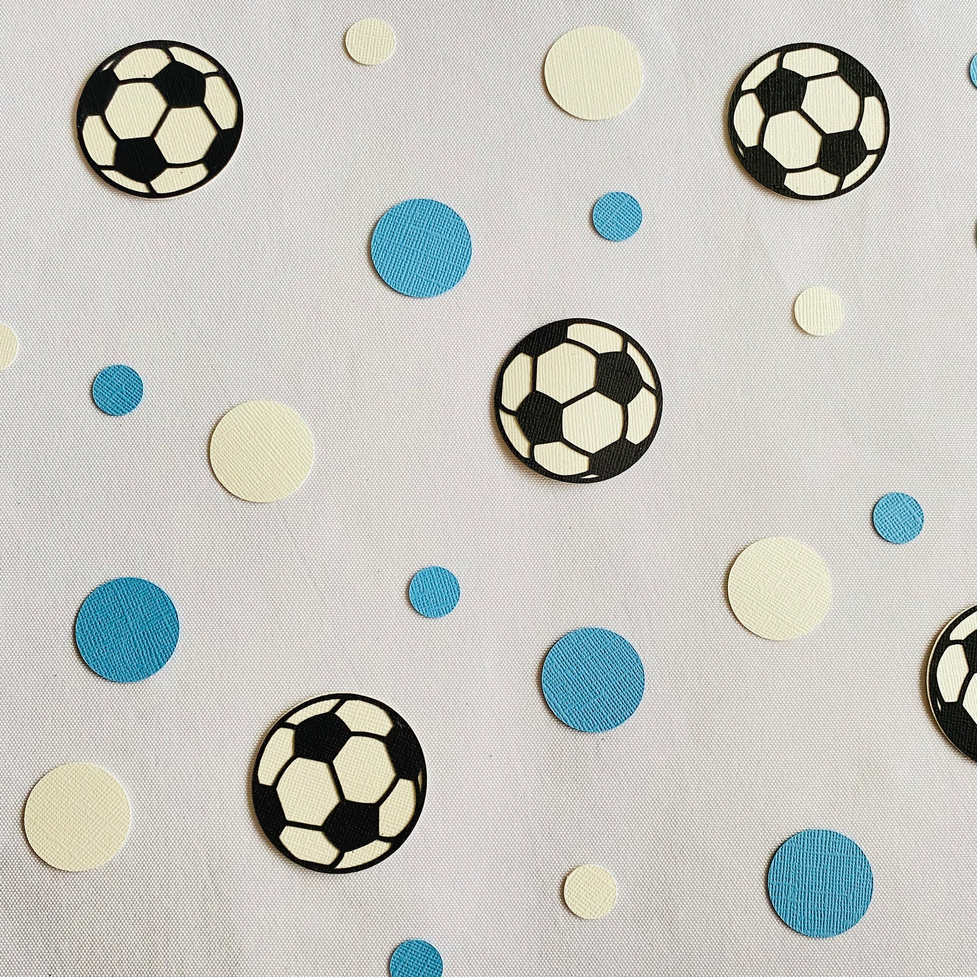 Blue and white round paper cutouts with soccer ball cutouts spread on synthetic grass