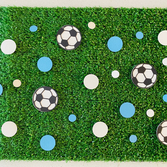 Blue and white round paper cutouts with soccer ball cutouts spread on synthetic grass