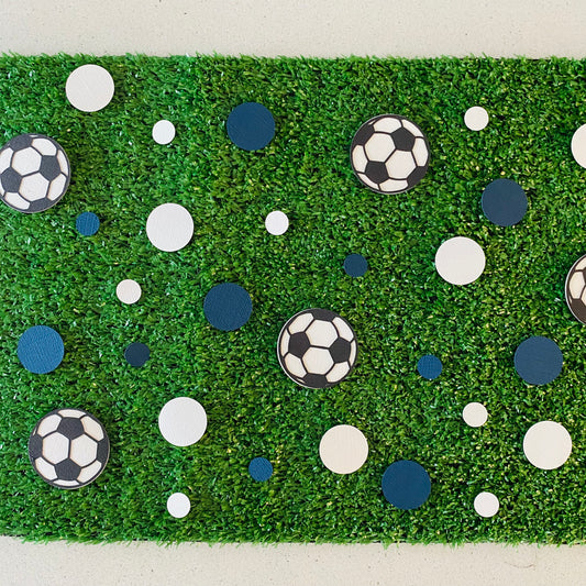 Blue and white round paper cutouts with soccer ball cutouts spread on synthetic grass