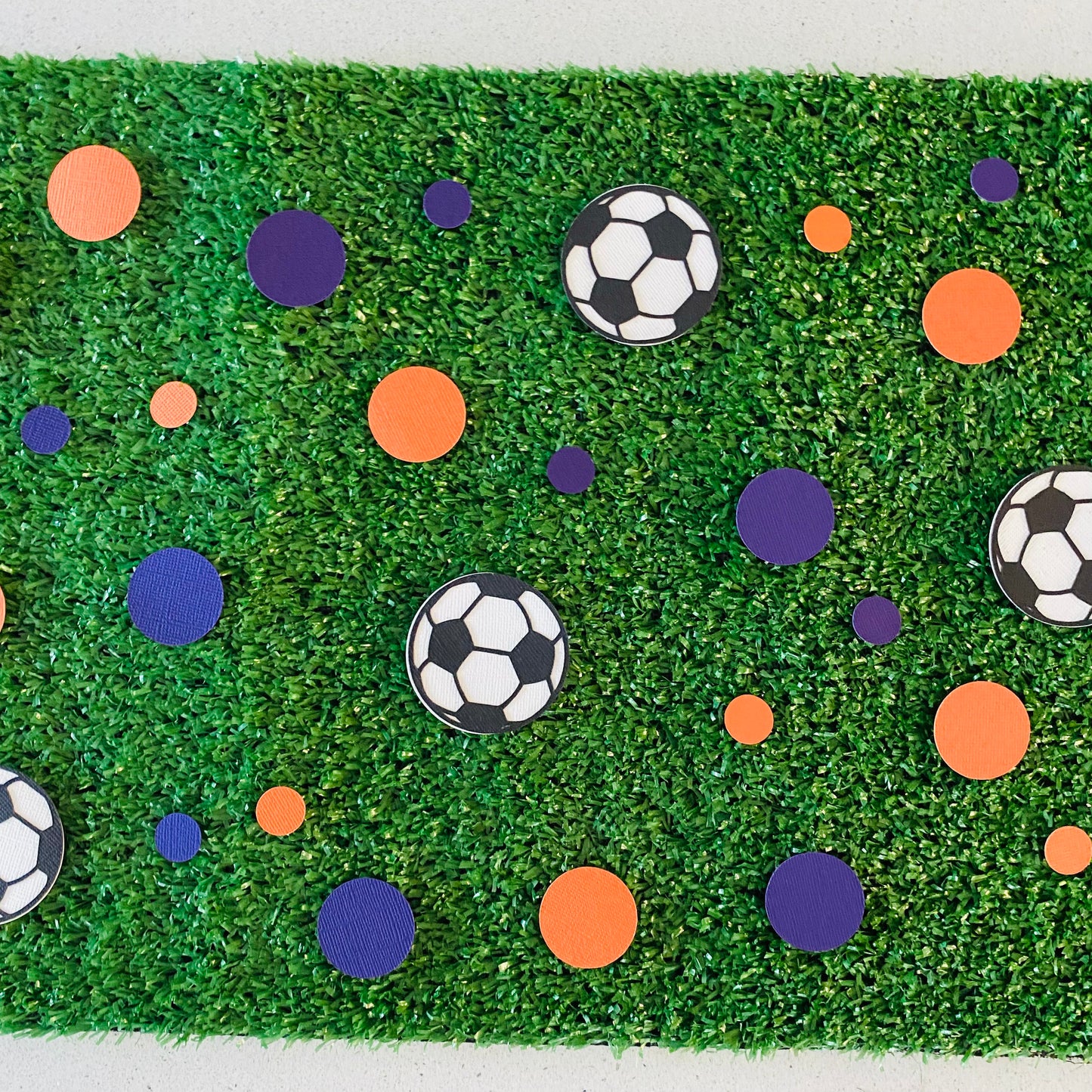 Blue and orange round paper cutouts with soccer ball cutouts spread on synthetic grass
