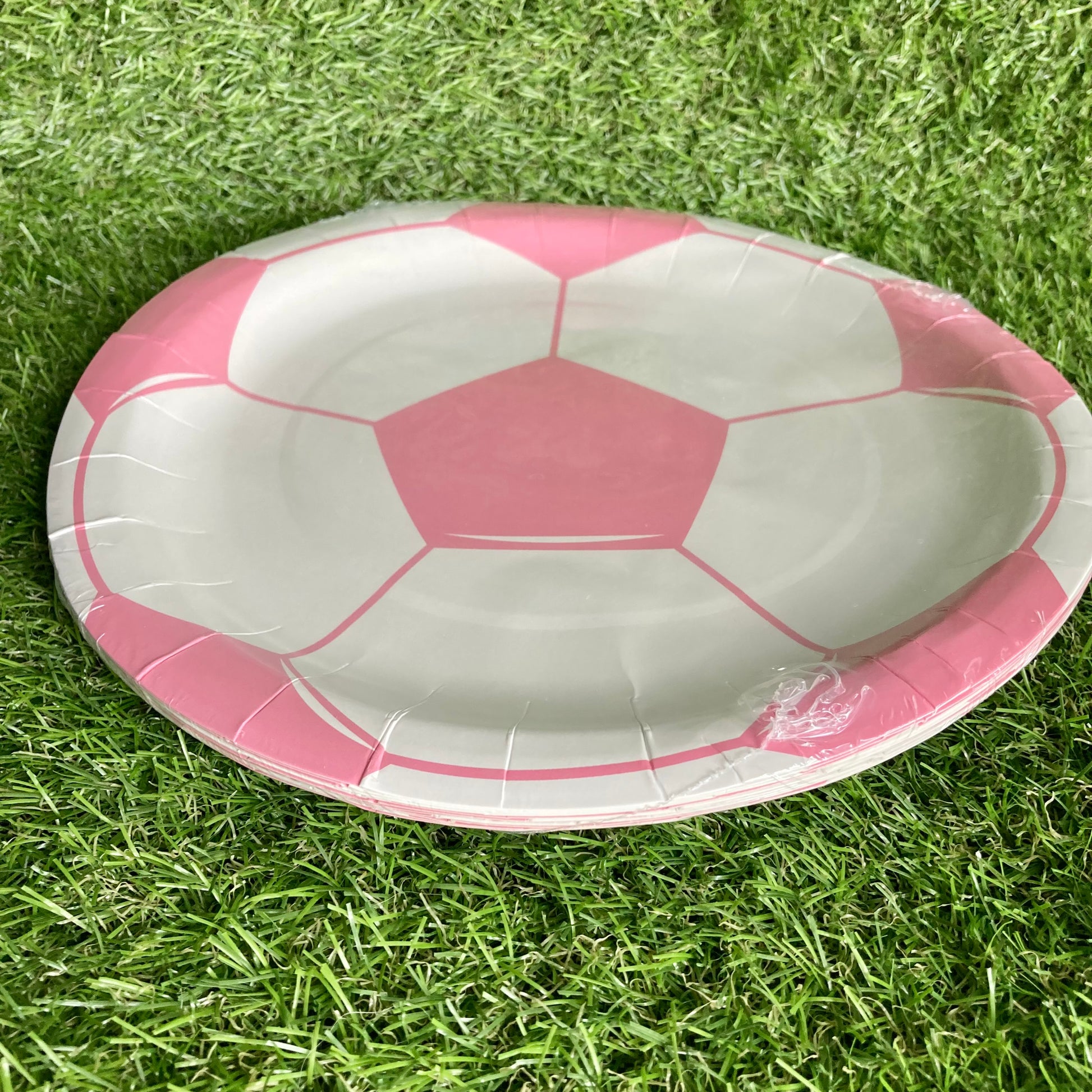 Side view of Pink soccer ball theme paper cake plate displayed on astro turf green grass.