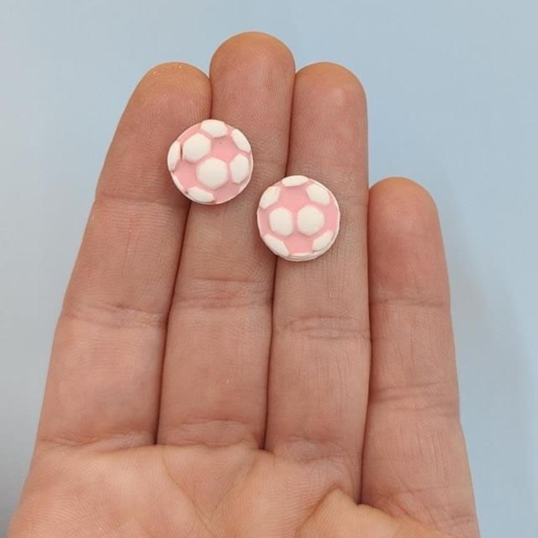 Pink and white soccer ball stud earrings laying on a hand for size comparison.