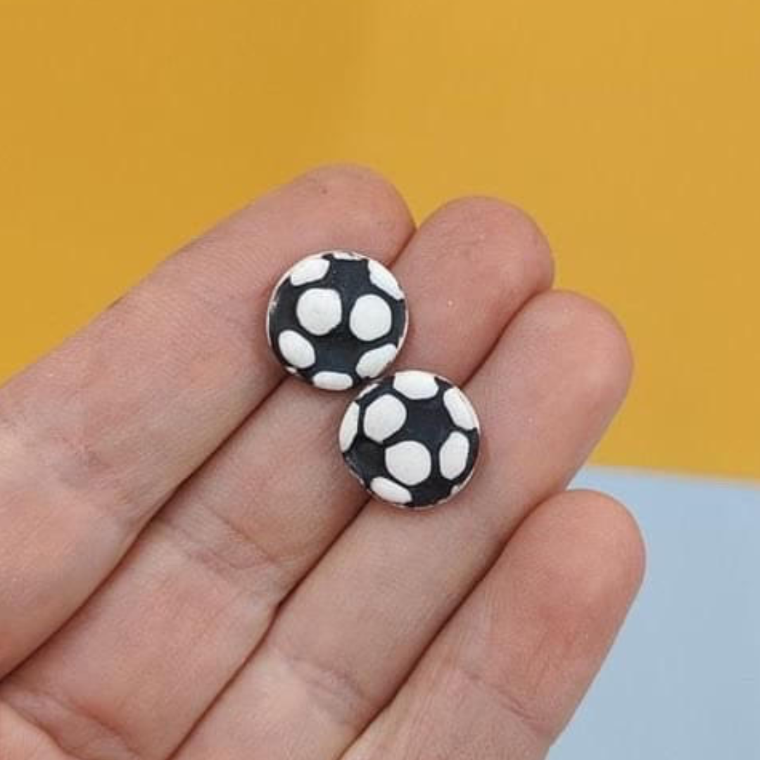 Black and white stud soccer ball earrings laying on a hand for size comparison.