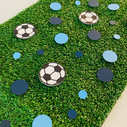 Dark Blue and Light Blue round paper cutouts with soccer ball cutouts spread on synthetic grass