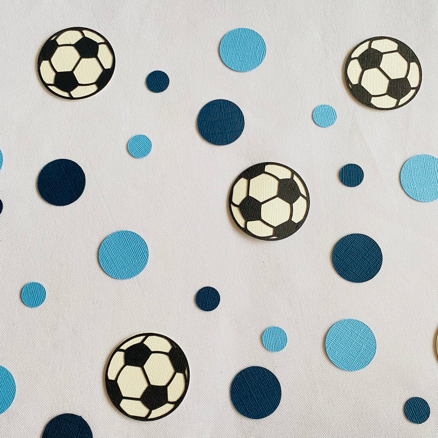 Dark Blue and Light Blue round paper cutouts with soccer ball cutouts spread on synthetic grass