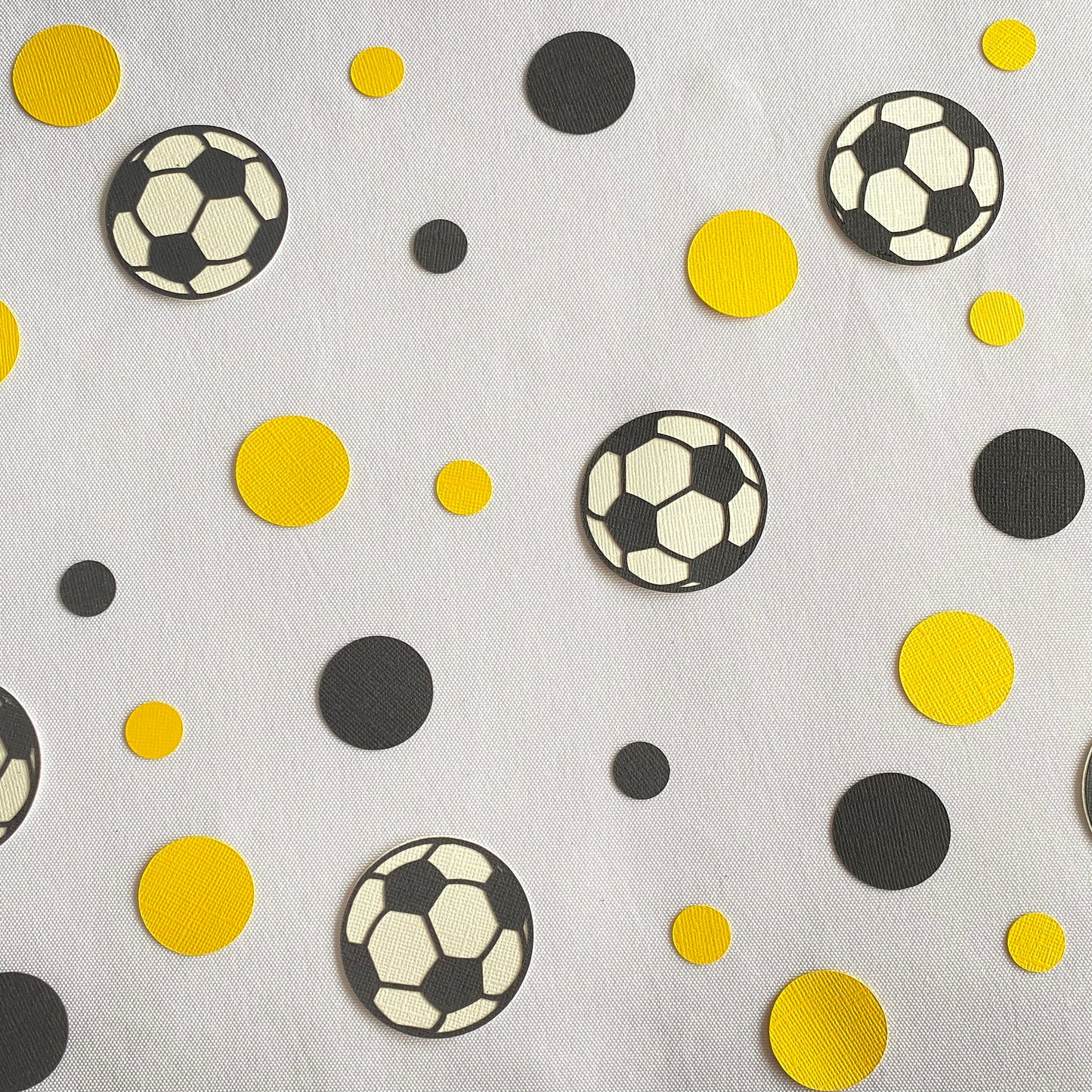 Yellow and Black small and large papercut circles with black and white soccer balls scattered across a white table